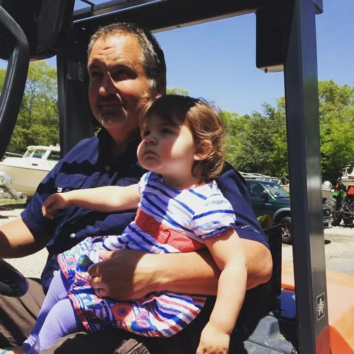 Owner holding a child at the helm of a work vehicle at the yard